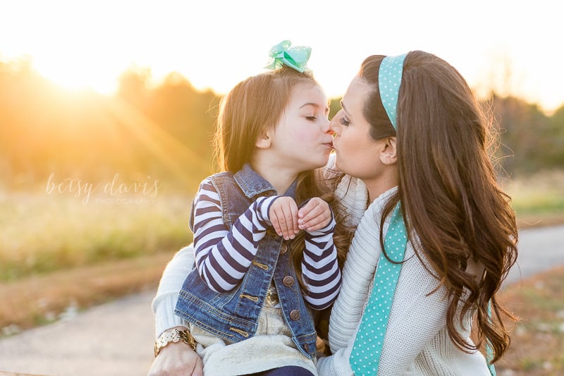 mother and daughter kissing with sun flare behind them
