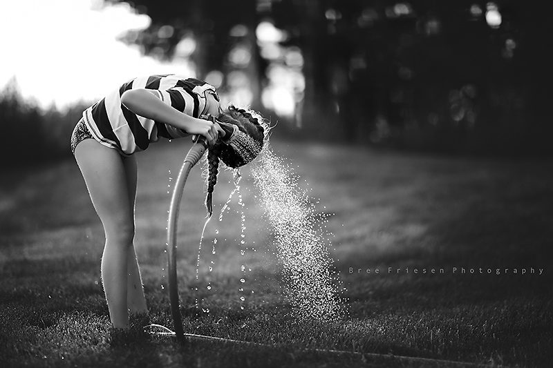 black and white photo of girl washing hair with water hose