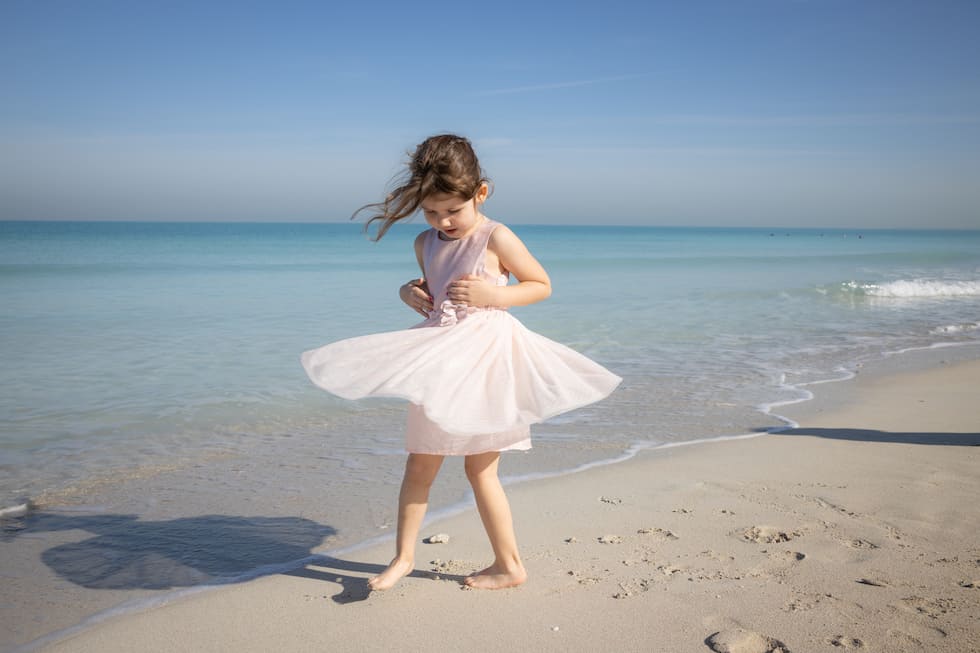 little girl in pink dress twirling on the beach