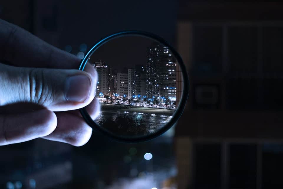 man holding lens filter showing buildings at night 