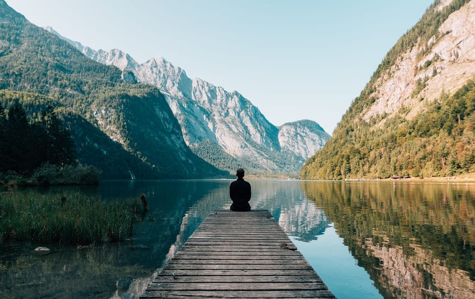 man sitting on dock with mountains in the background