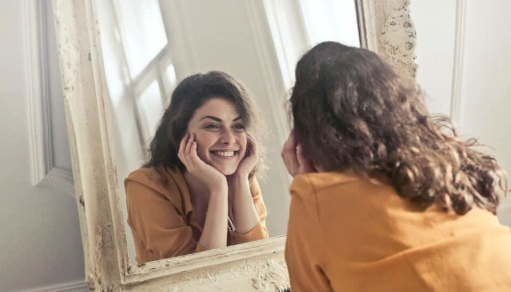 woman in yellow shirt looking at herself in a mirror