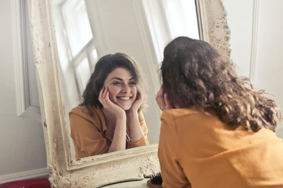 woman in yellow shirt looking at herself in a mirror