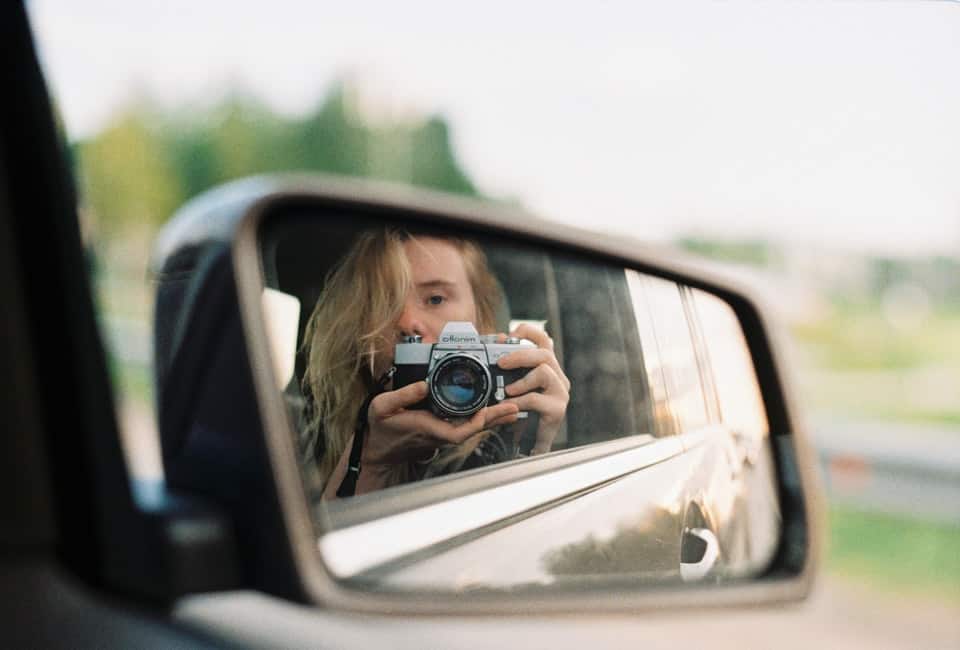 girl in rearview mirror holding camera