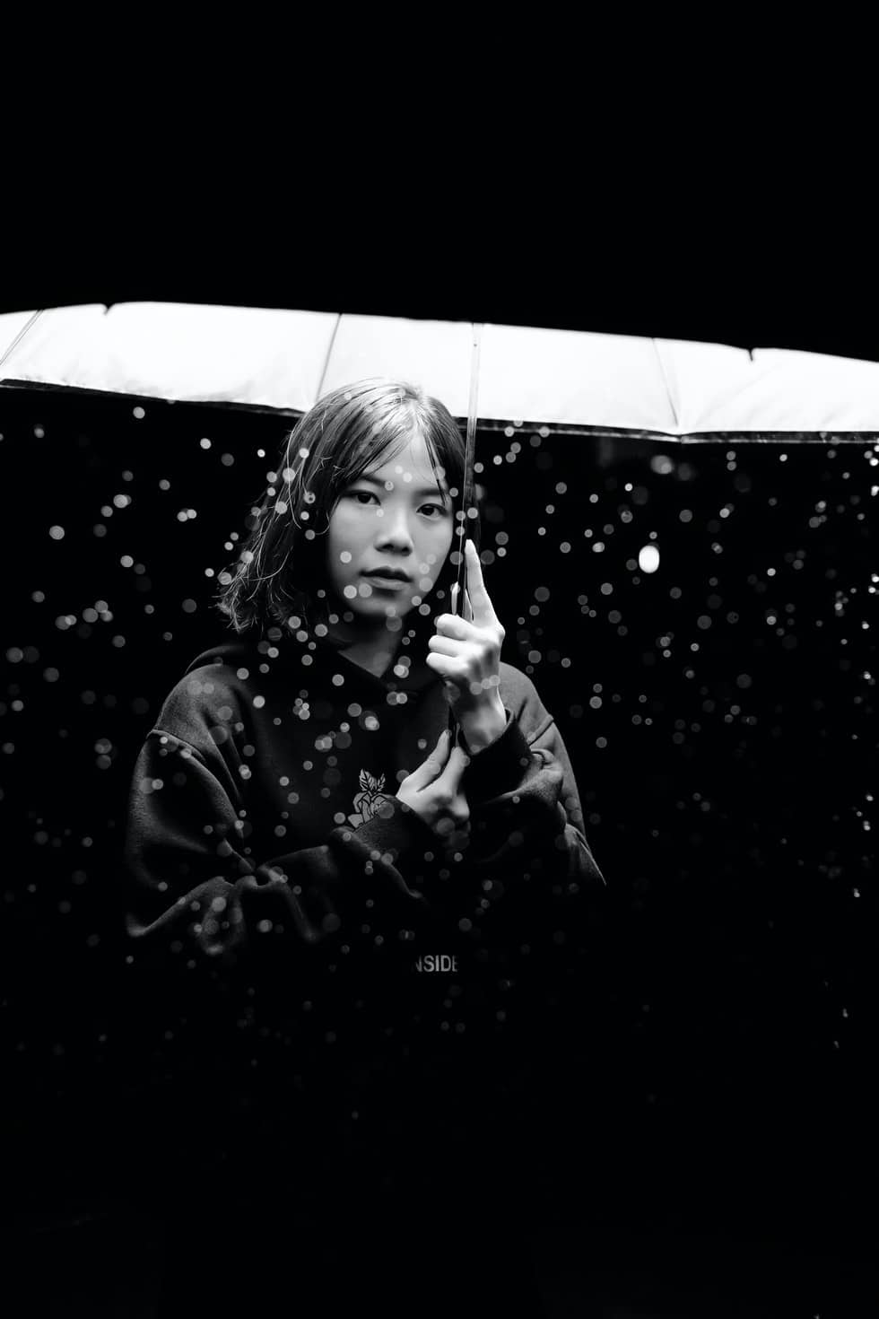 black and white photo of woman in rain holding an umbrella